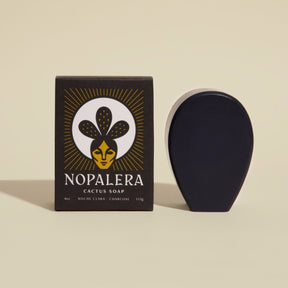 An oval shaped black bar soap stands to the right of its black rectangular packaging. This cactus soap contains a subtle scent of eucalyptus and sage oil with activated charcoal. Noche Clara Cactus Soap is from Nopalera and made in Brooklyn, NY.