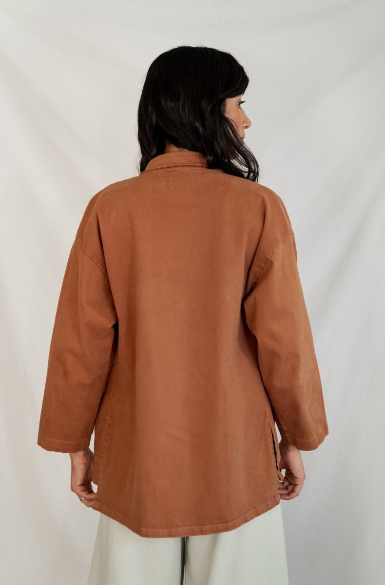 Model shows the back side of a chore jacket with off-white buttons and two oversized pockets in the color Saddle Brown. The Painter's Jacket is designed by Mien and made in Los Angeles, CA.