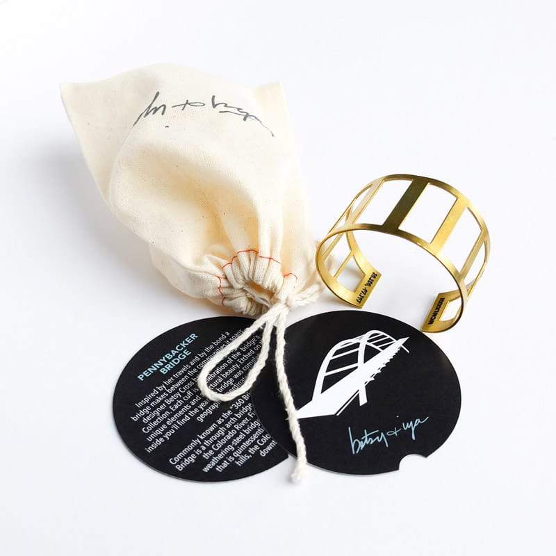 Betsy & iya's Pennybacker Bridge cuff, pictured with a muslin storage pouch, an informational card about the bridge, and a cuff care card. Hand-crafted in Portland, Oregon.