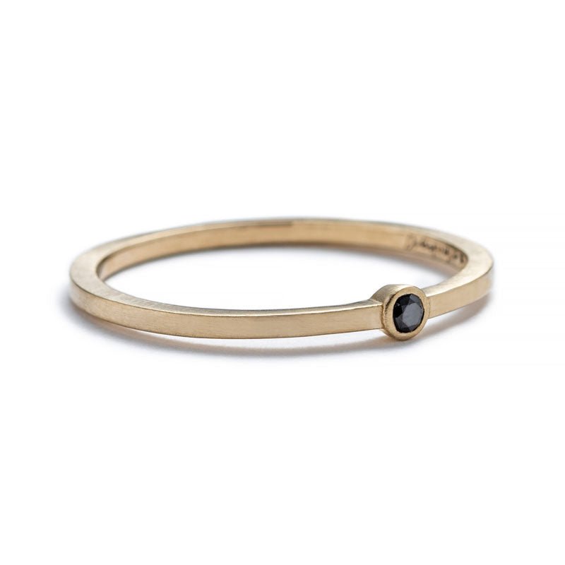 Thin, 14k yellow gold band with a matte finish, featuring a small, round, bezel-set black diamond, and engraved on the inner band with the betsy & iya logo. Hand-crafted in Portland, Oregon.