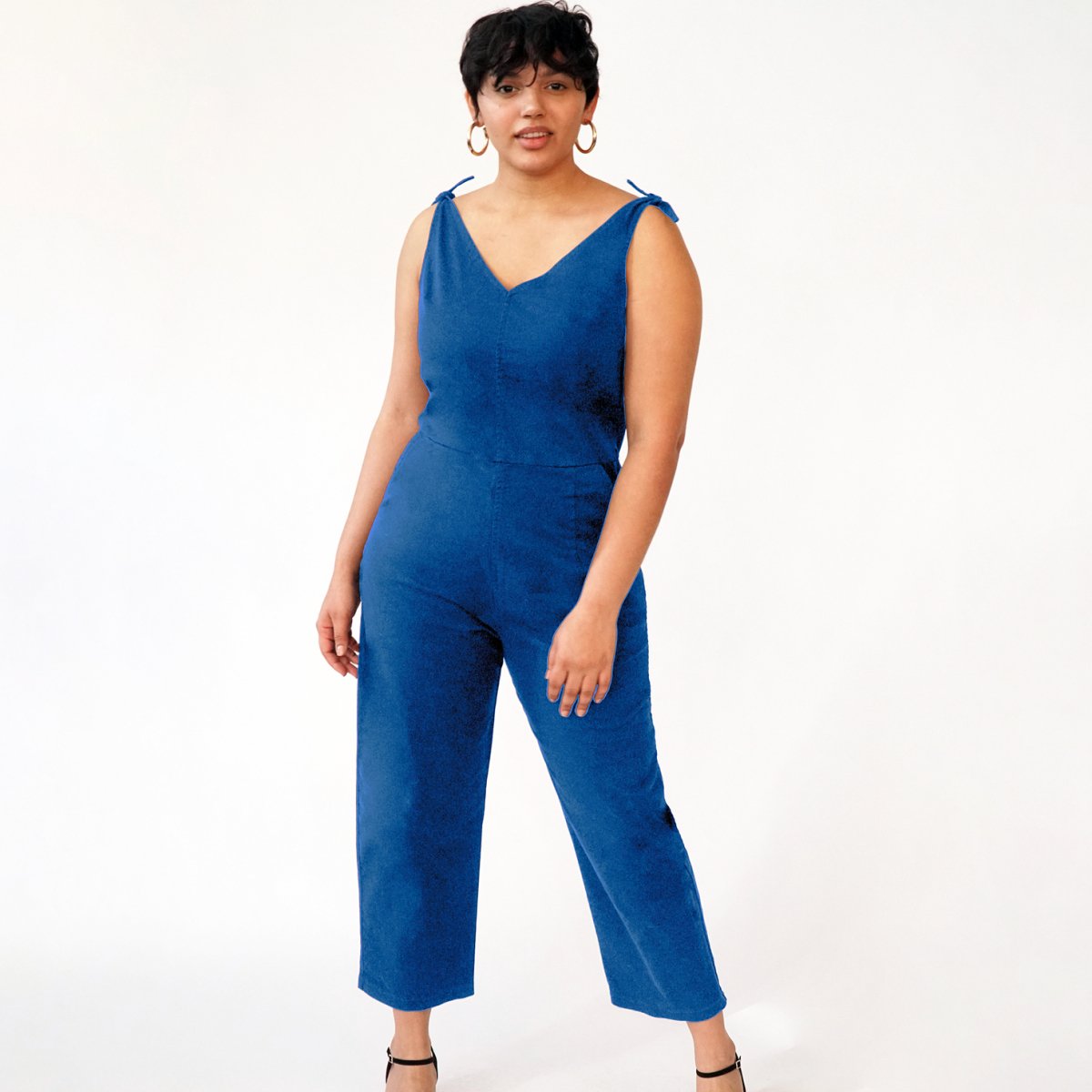 Model wears a bright blue colored jumpsuit with a V-neckline and tie up shoulder straps. The Slate Overalls in Royal are designed by Loup and made in New York City, USA.