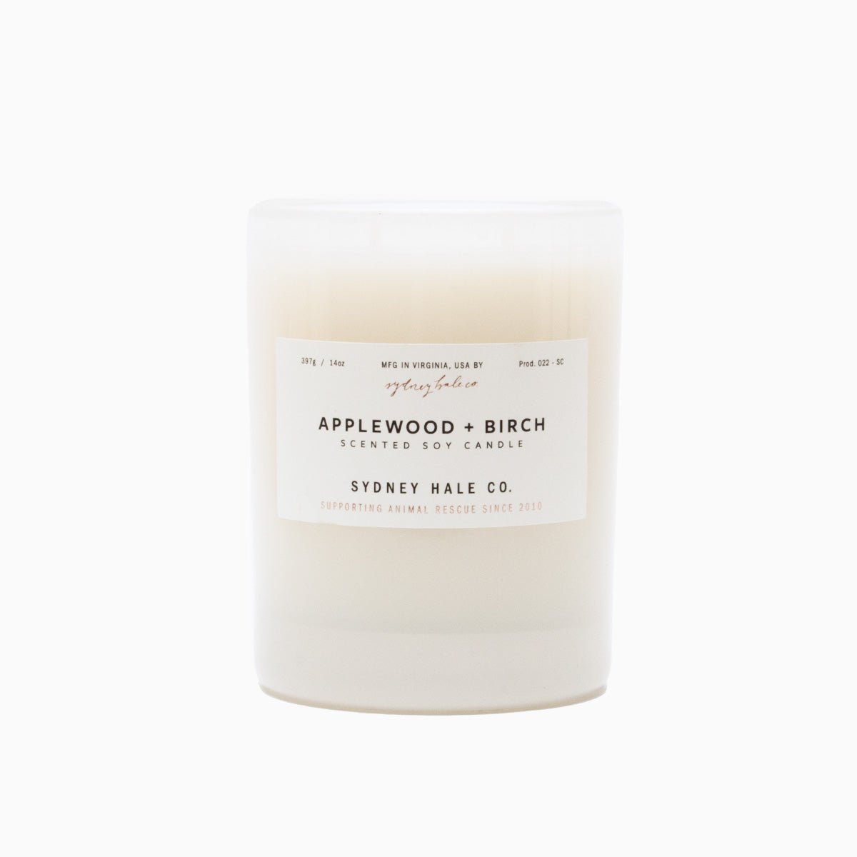 A cylindrical glass candle filled with a soy wax blend and two double cotton wicks. Label reads: "397g/14 oz. Manufactured in Virginia, USA by Sydney Hale Co. Applewood + Birch scented soy candle. Sydney Hale Co. Supporting Animal rescue since 2010."