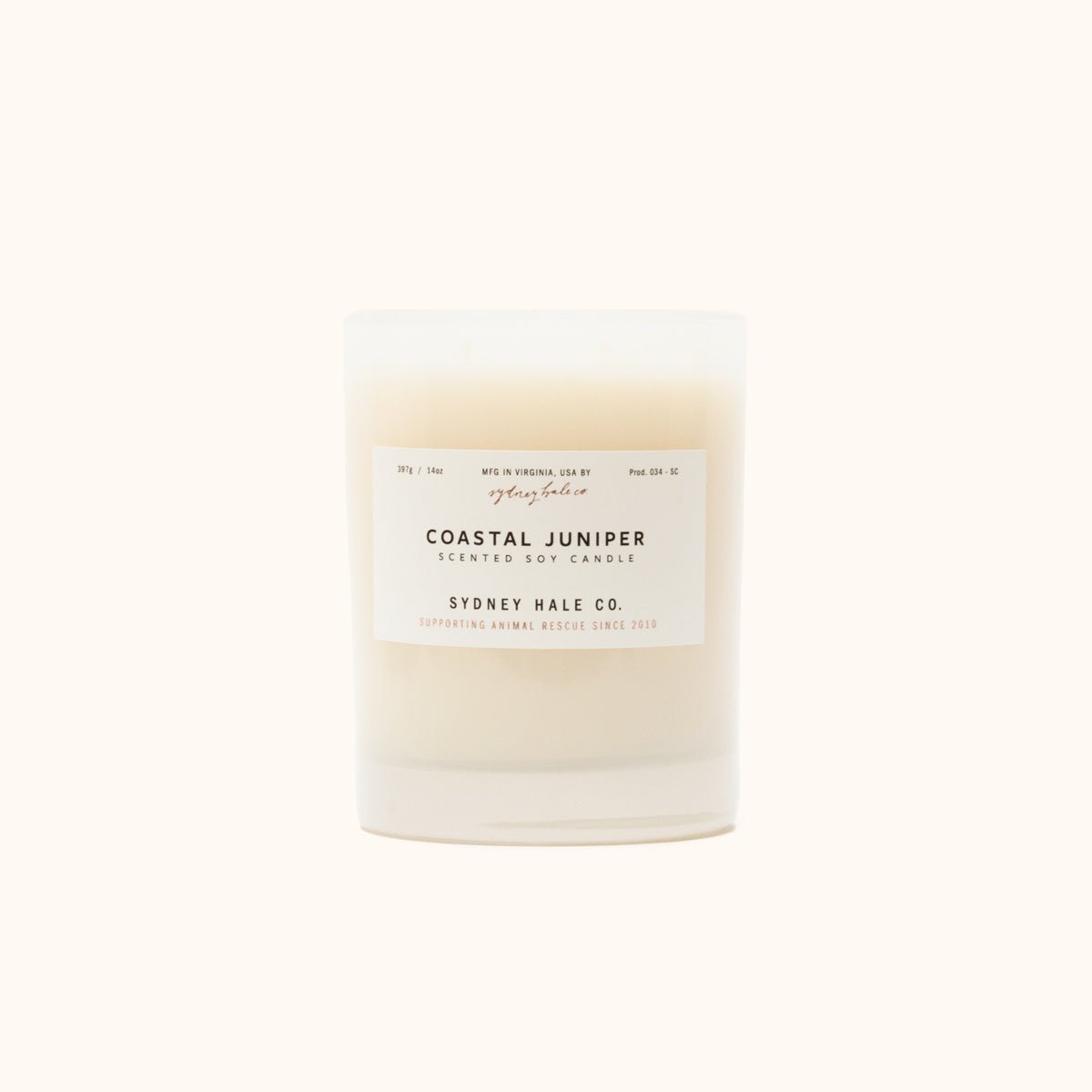 A cylindrical glass candle filled with a soy wax blend and two double cotton wicks. Label reads: "397g/14 oz. Manufactured in Virginia, USA by Sydney Hale Co. Coastal Juniper scented soy candle. Sydney Hale Co. Supporting Animal rescue since 2010."