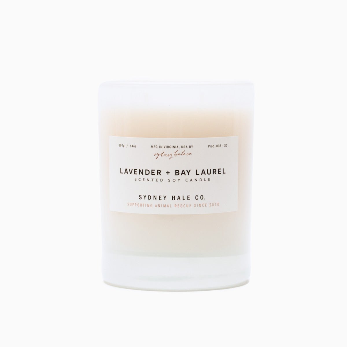 A cylindrical glass candle filled with a soy wax blend and two double cotton wicks. Label reads: "397g/14 oz. Manufactured in Virginia, USA by Sydney Hale Co. Lavender + Bay Laurel scented soy candle. Sydney Hale Co. Supporting Animal rescue since 2010."