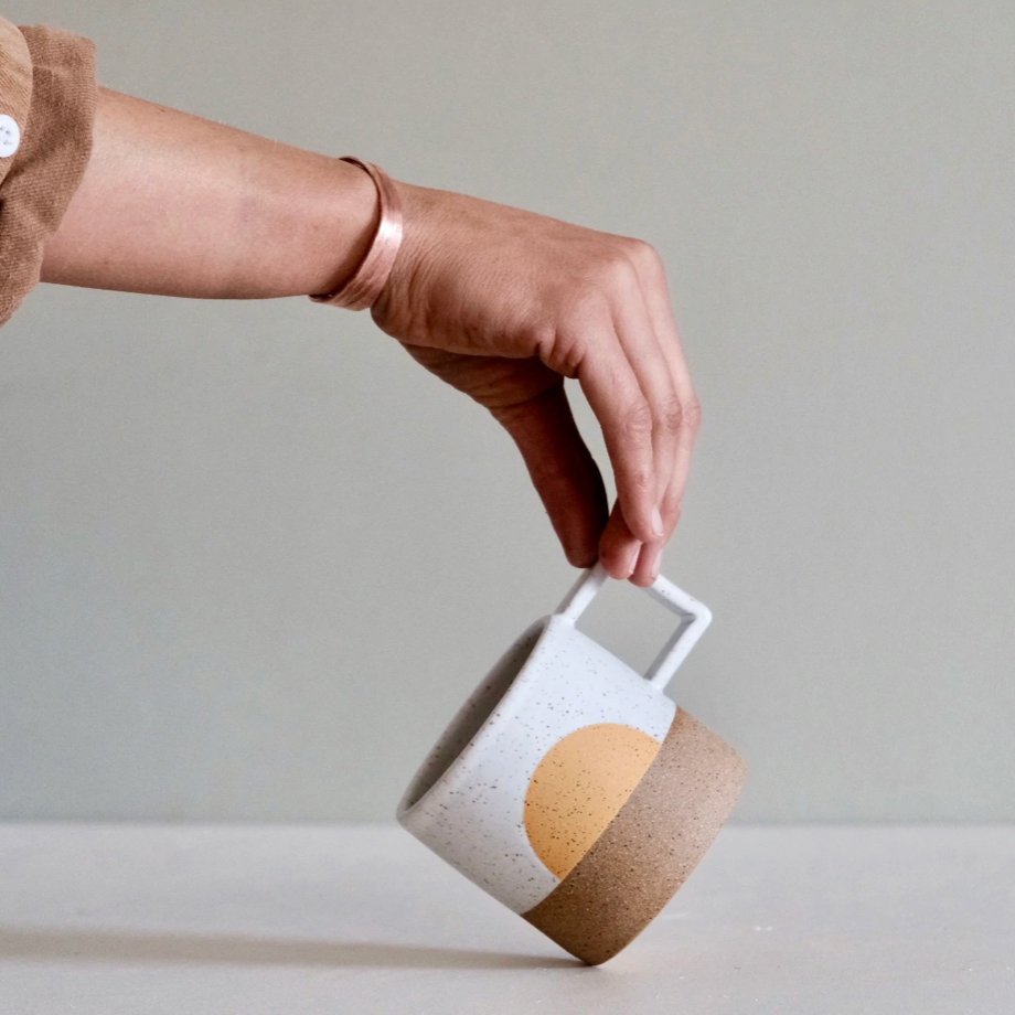 A mug with a white speckled and natural clay finish with a half moon design in a warm yellow. The Speckled Sunrise Mug is designed and handmade by Wolf Ceramics in Hood River, Oregon.