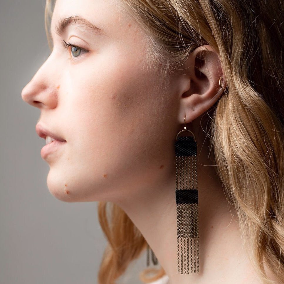 Model wears Two tier black beaded dangle earrings connected by strands of antique brass chains. Designed and handmade by A Nod To Design in Portland, Oregon.