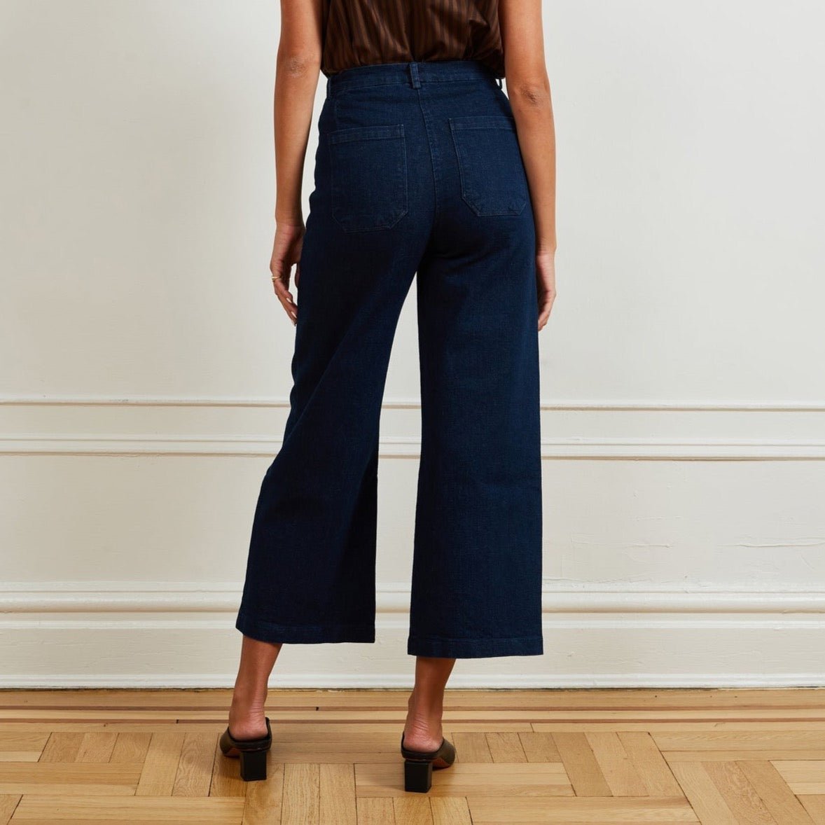 A model shows the backside of a high waisted wide leg cropped jean in a dark blue denim. The Simone Jean in Dark Indigo is designed by Loup and made in New York City, USA.