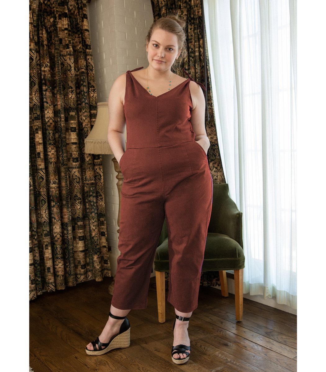 Model wears a rusty red colored jumpsuit with a V-neckline and tie up shoulder straps. The Slate Overalls in Terracotta are designed by Loup and made in New York City, USA.