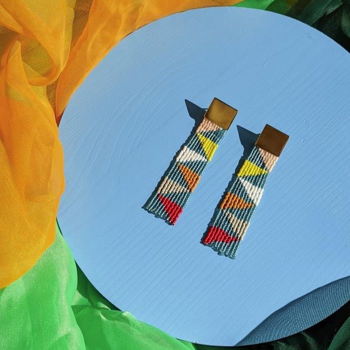 Beaded fringe earrings with a brass square stud. Beads are in emerald, white, yellow, red, grey, orange and salmon. They create a triangular pattern throughout. The Small Kaleidoscope Beaded earrings are designed and handmade by Take Shape Studio in Berkley, California.