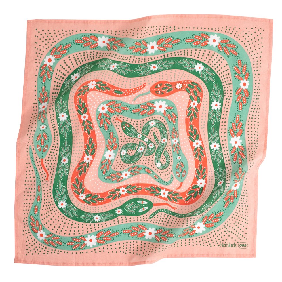 A pink bandana with a green, white and red floral snake pattern. Designed by Hemlock Goods in Fulton, MO and screen printed by hand in India.