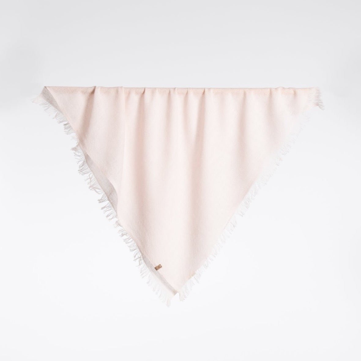 A square scarf made of 100% Merino wool in a light pink color. The Merino Square Woven Scarf in Blush Pink is designed by Dinadi and handcrafted in Nepal.