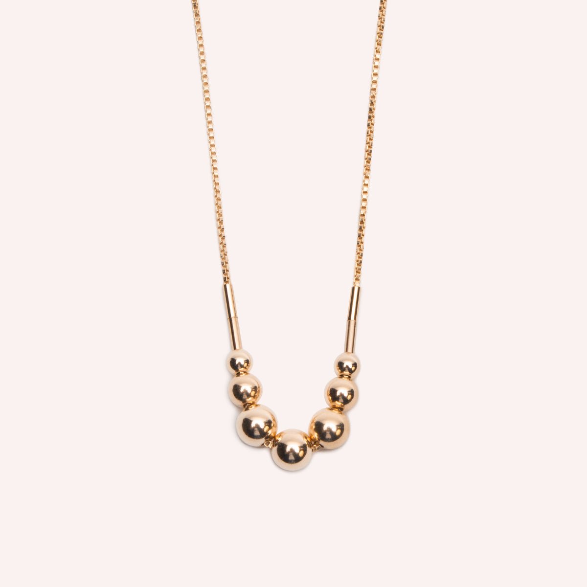 A gold fill necklace featuring a delicate chain and seven round beads flanked by narrow tube beads. The Strella Necklace is designed and handcrafted in Portland, Oregon.