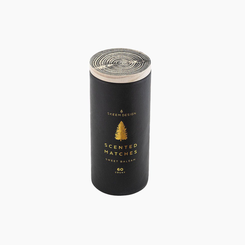Black cylindrical packaging with a gold tree design. Contains 60 scented matchstick in the scent sweet balsam. Made in Philadelphia, PA by SKEEM Design.