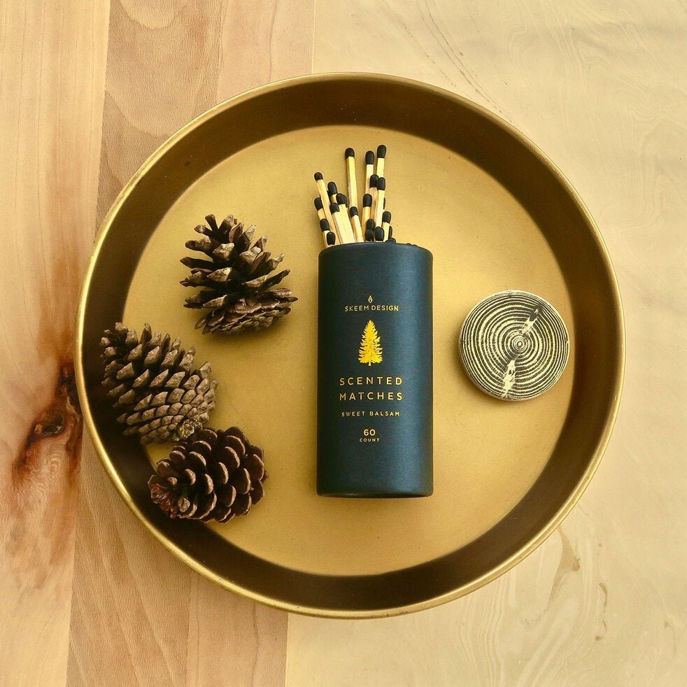 Black cylindrical packaging with a gold tree design. Contains 60 scented matchstick in the scent sweet balsam. Made in Philadelphia, PA by SKEEM Design.