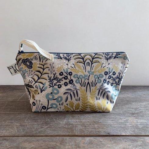 Cosmetic/accessory bag with delicate floral pattern in slate blue, navy, white, blush and metallic gold. Contains a blue zipper with a white twill zipper pull. Designed by Frankie & Coco and handmade in Portland, Oregon.