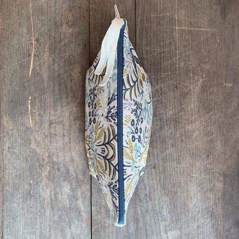 Cosmetic/accessory bag with delicate floral pattern in slate blue, navy, white, blush and metallic gold. Contains a blue zipper with a white twill zipper pull. Designed by Frankie & Coco and handmade in Portland, Oregon.