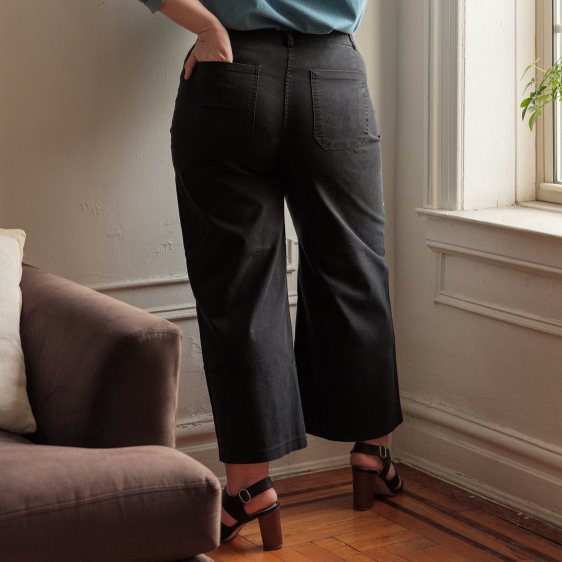 A model shows the backside of a wide leg black pant with zipper fly. The Toni Jeans in Black are designed by Loup and made in New York City, USA.