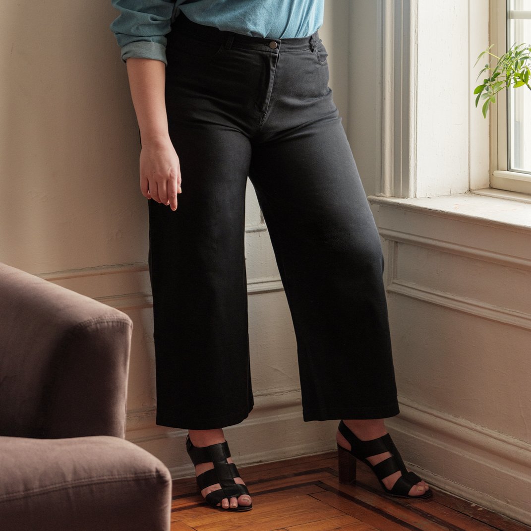 A model wears a wide leg black pant with zipper fly. The Toni Jeans in Black are designed by Loup and made in New York City, USA.
