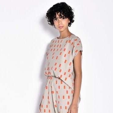 A short sleeve light grey tunic with an orange square pattern. The Tunic in Orange Disko is designed and sewn by Uzi NYC in Brooklyn, New York.