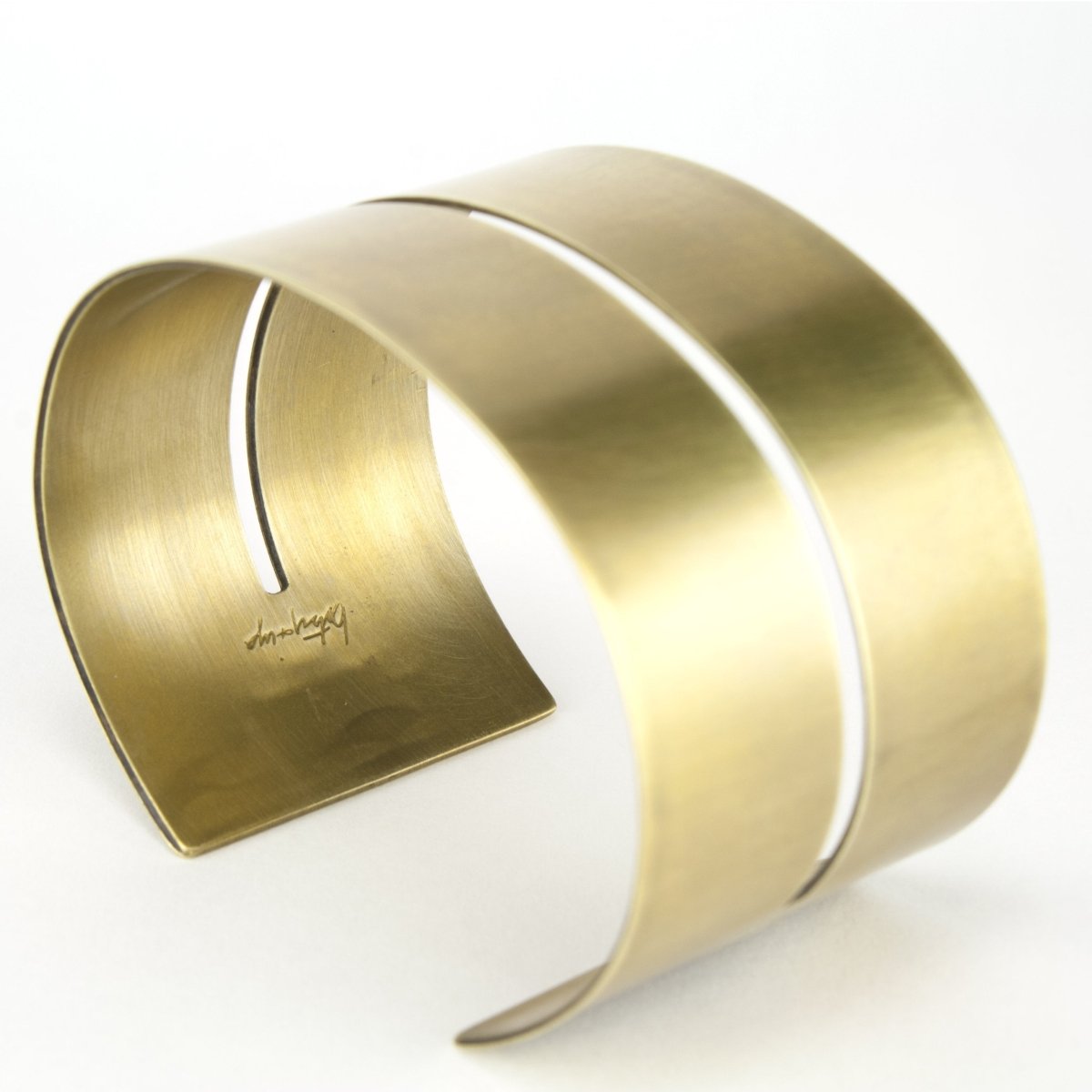 Wide, bold, brass cuff bracelet with a cutout that runs through the center of the cuff and stops just short of either end of the cuff, with the betsy & iya logo engraved on the inside. Hand-crafted in Portland, Oregon.