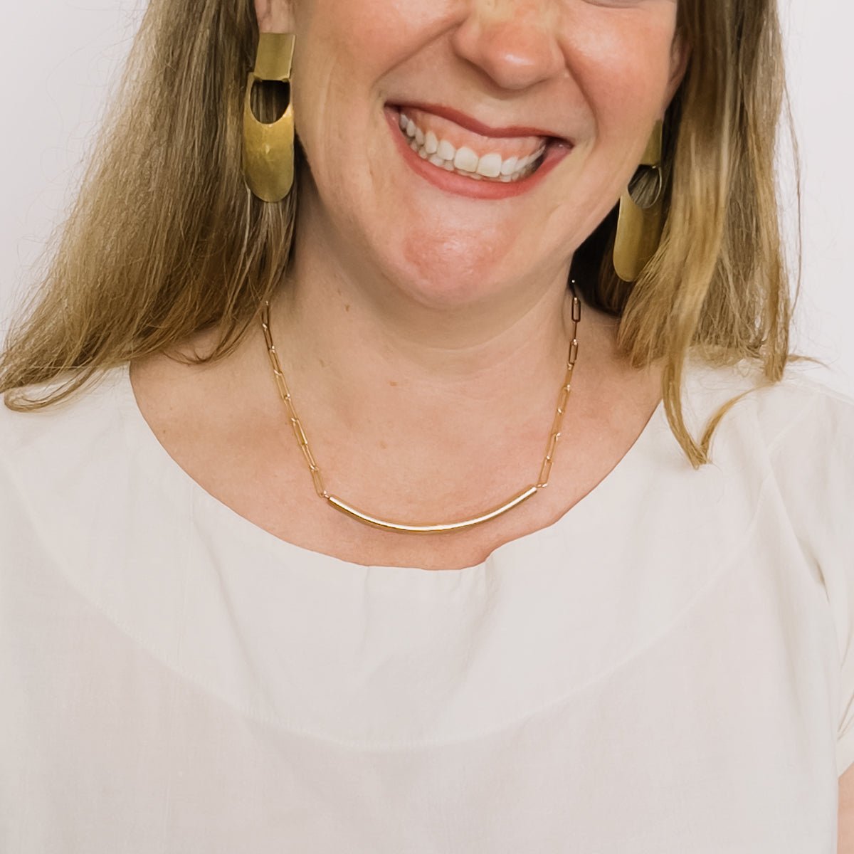 A model wears a gold fill chain necklace with a cylindrical curved focal bar. The Virada Necklace is Designed and handcrafted in Portland, Oregon.