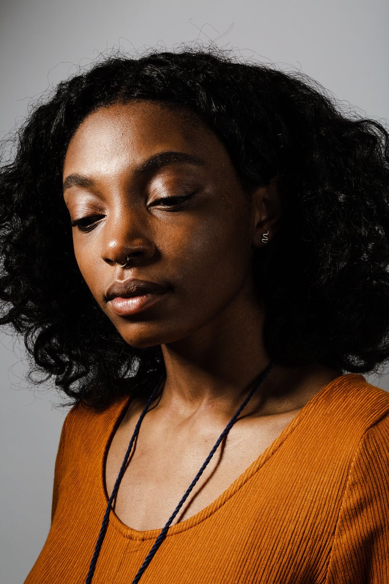 Tiny, silver, snake-inspired studs, worn by a model with curly black hair and an ochre dress.