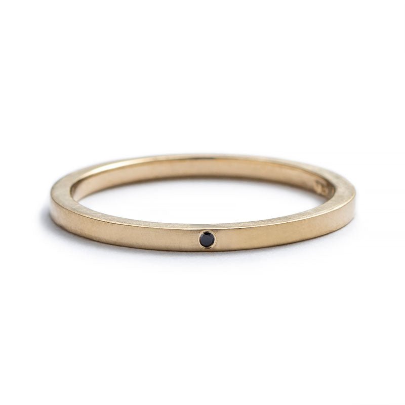 Thin, 14k yellow gold stacking band with a matte finish, and a tiny, round, flush-set black diamond. Hand-crafted in Portland, Oregon.