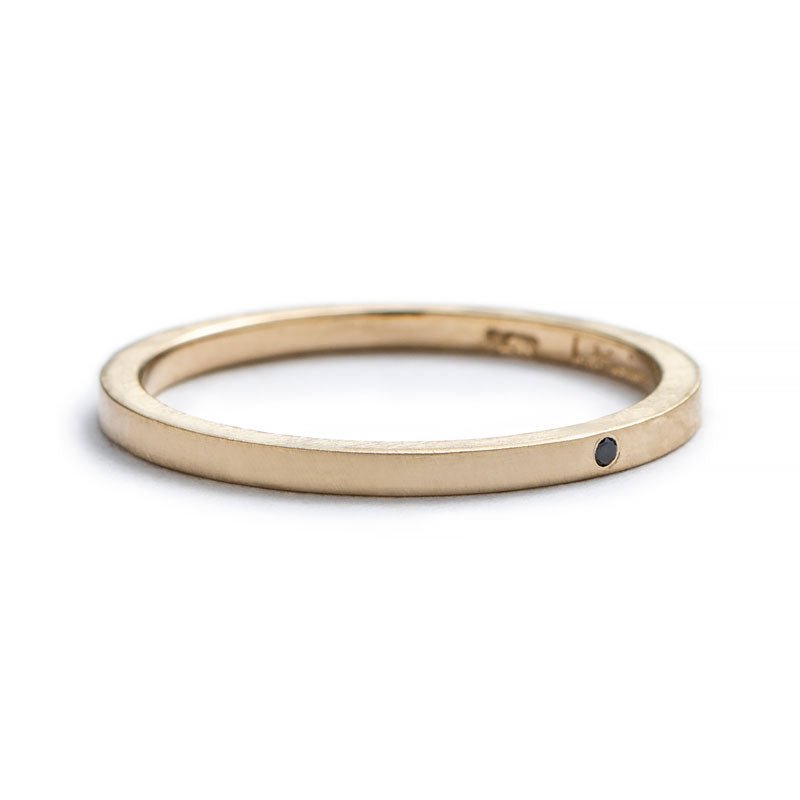 Thin, 14k yellow gold stacking band with a matte finish, a tiny, round, flush-set black diamond, and the betsy & iya logo engraved on the inner band. Hand-crafted in Portland, Oregon.