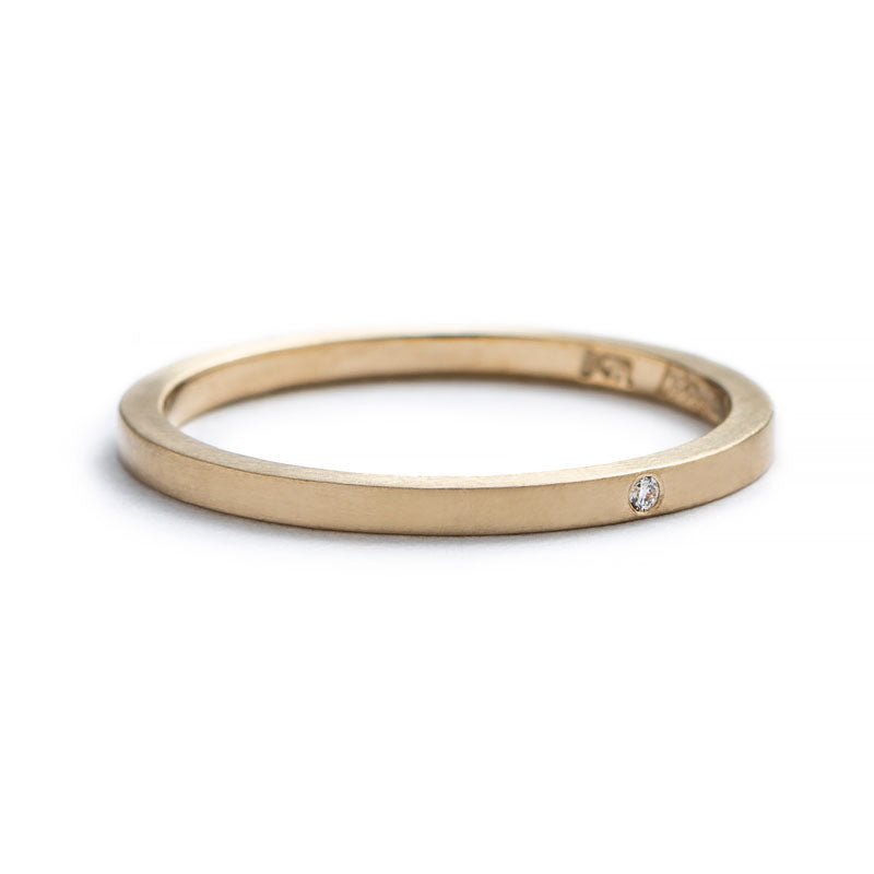 Thin, 14k yellow gold stacking band with a matte finish, a tiny, round, flush-set white diamond, and the betsy & iya logo engraved on the inner band. Hand-crafted in Portland, Oregon.