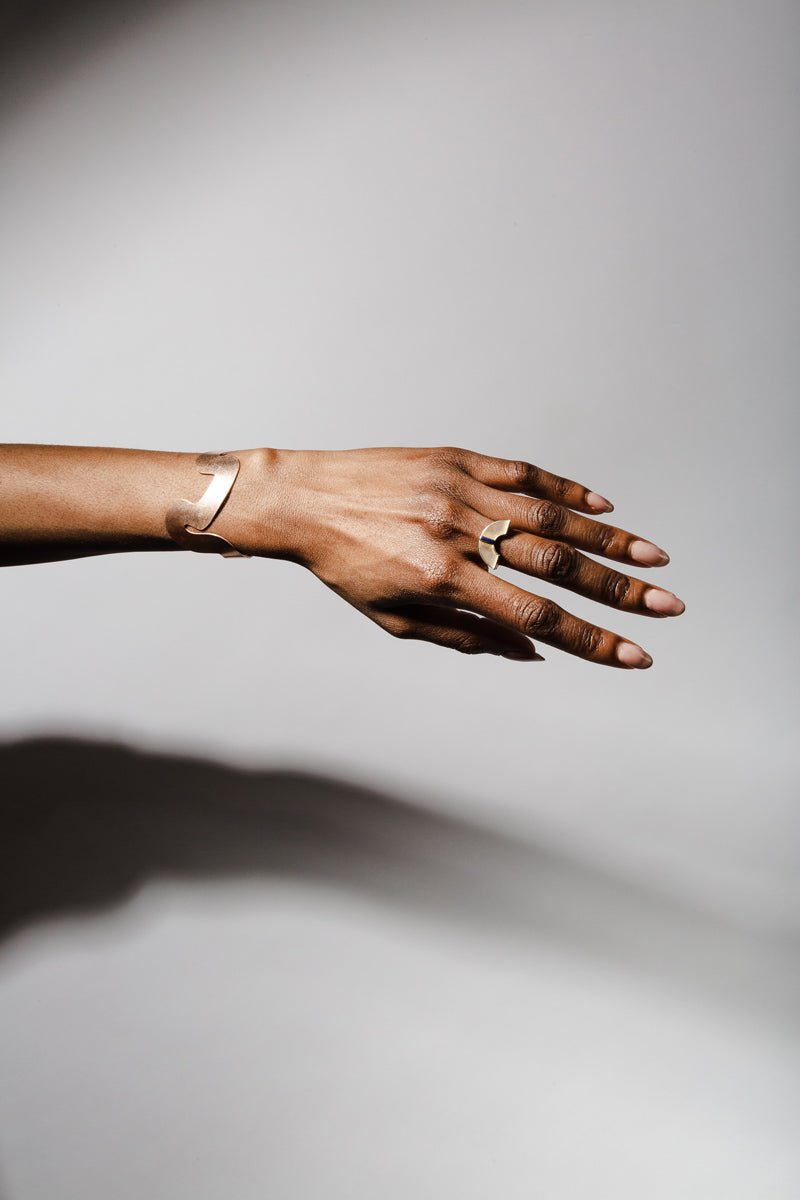 The bronze Willamette cuff bracelet and bronze and lapis lazuli betsy & iya Forti ring, styled together on a model's wrist and hand.