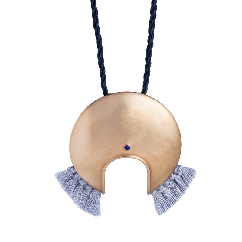 Large, circular, cast-bronze focal piece, featuring a u-shaped cutout at the bottom of the circle, a blue, bezel-set, lapis lazuli stone, and periwinkle cotton fringe, threaded with an adjustable, navy blue cotton cord. Hand-crafted in Portland, Oregon.