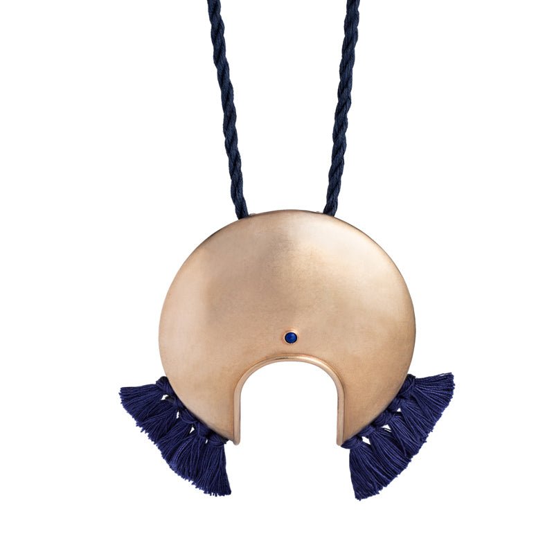 Large, circular, cast-bronze focal piece, featuring a u-shaped cutout at the bottom of the circle, a blue, bezel-set, lapis lazuli stone, and navy blue cotton fringe, threaded with an adjustable, navy blue cotton cord. Hand-crafted in Portland, Oregon.