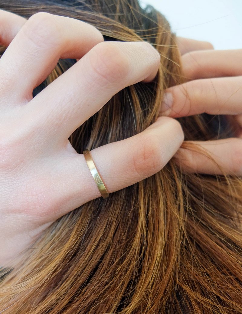 Thin, flat, 14k yellow gold Amandi band with a matte finish, worn on a model's little finger.