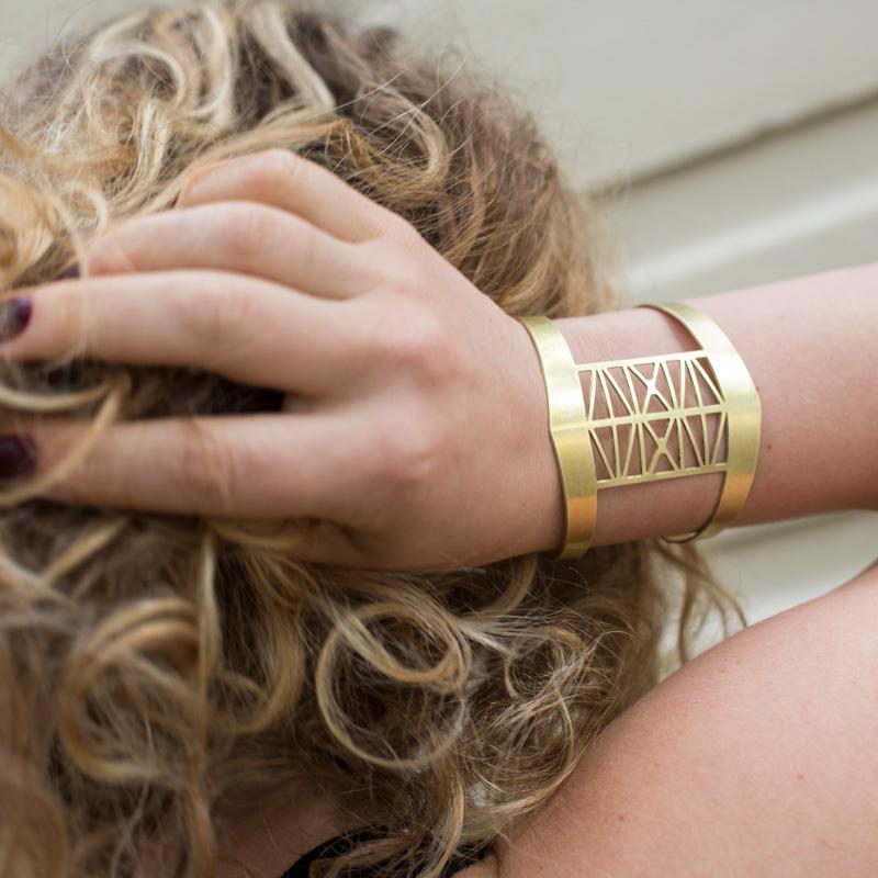 The brass Steel Bridge cuff bracelet by betsy & iya, pictured on the wrist of a model with curly, blonde hair.