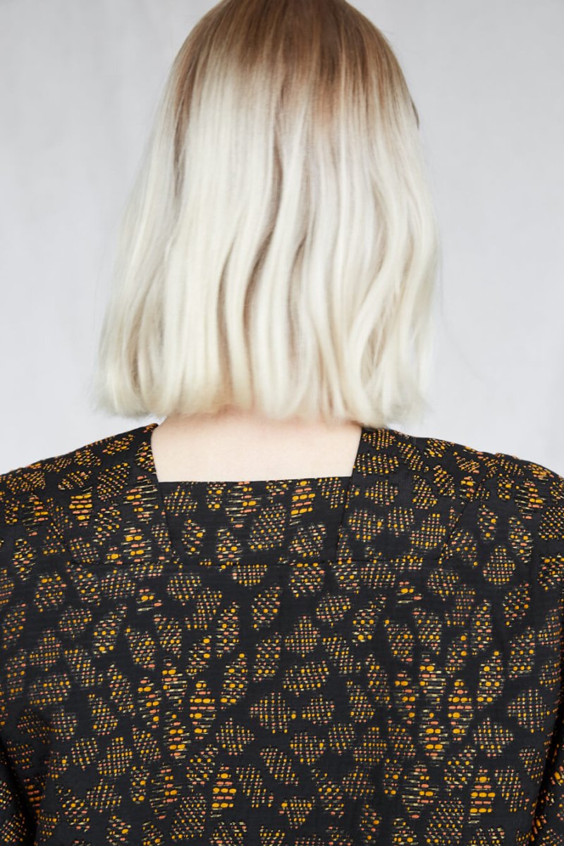 Blonde woman faces away while wearing an orange and black dress with a square neckline. The Forsaken Love Dress is from Canadian designer Eve Gravel.