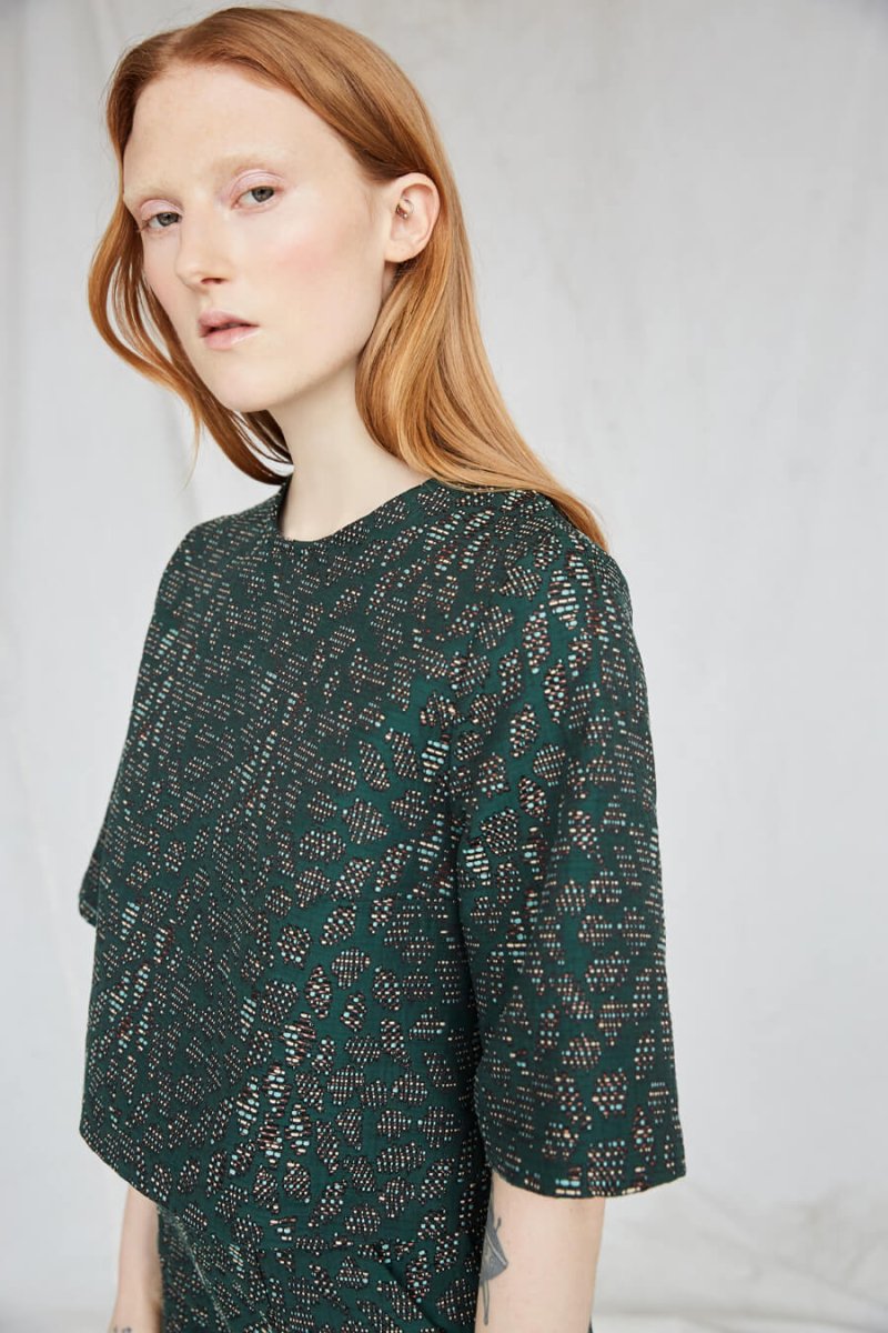 Red-haired woman wears an emerald top with intricate jacquard detailing. The Night Bird top is from Canadian designer Eve Gravel.