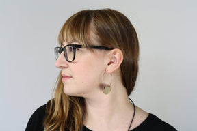 Betsy & iya 14k gold-plated Novi hoop earrings, pictured on the profile of a model with sandy-blond bangs and glasses.