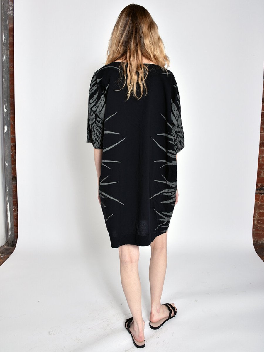Model shows backside of short black dress with three-quarter sleeves and light grey feather pattern on sides. Designed and sewn by UZI in Brooklyn, New York.