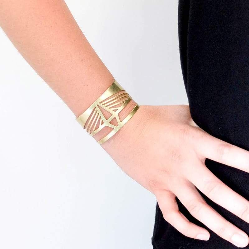 The front of the bold, modern, and adjustable brass Ravenel cuff bracelet, worn snugly on the wrist of a betsy & iya model.