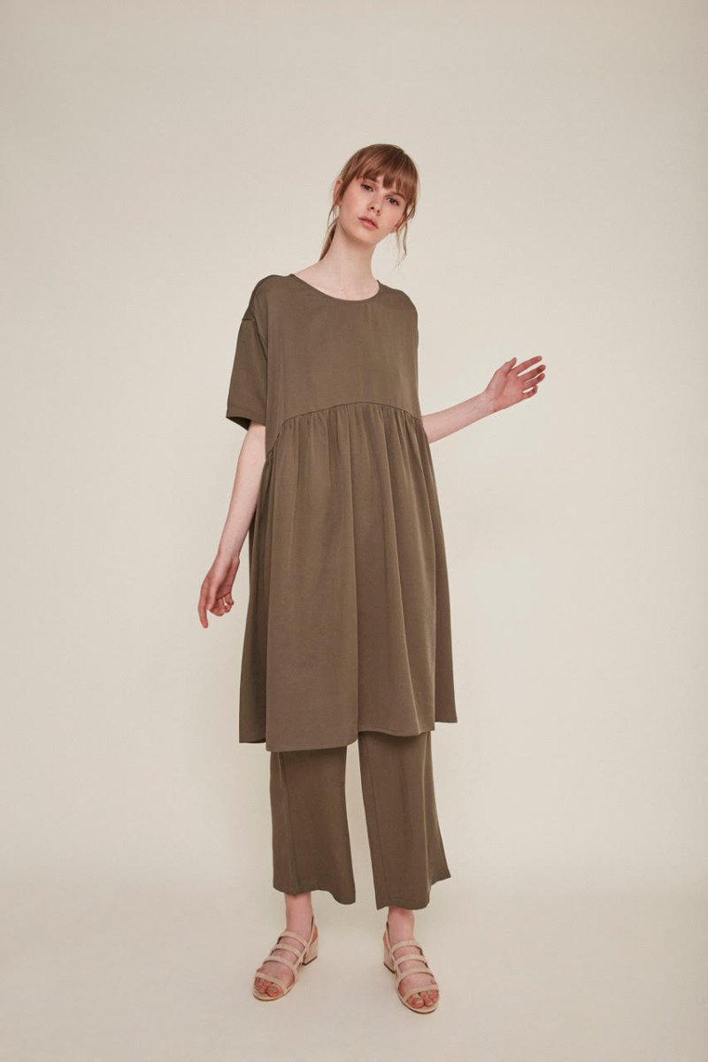 Red-haired woman wears a brown babydoll dress and matching pants. The Drapey Dress in Kaki is from designer Rita Row.