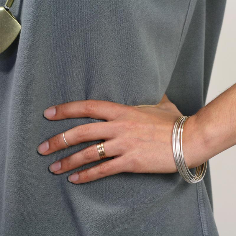 A stack of Betsy & Iya faceted gold-filled rings, styled on a model with a stack of sterling silver Lita bangles and a smooth silver knuckle ring.