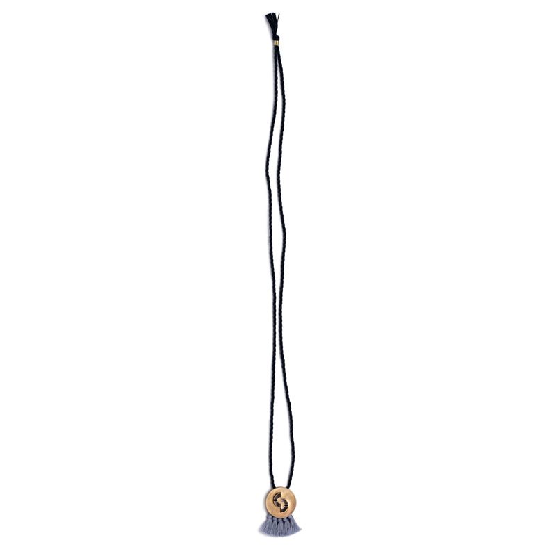 Circular, quarter-sized, cast-bronze pendant with curved cutouts, two rectangular, lapis lazuli inlays, and periwinkle cotton fringe, threaded with an adjustable, navy blue cotton rope. Hand-crafted in Portland, Oregon.