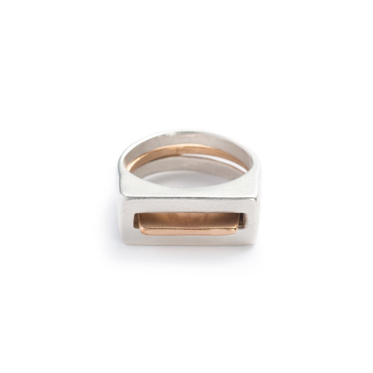 A pair of contemporary rings, featuring one thin, bronze ring with an elongated curve (Tuyo) fitted through a chunky, silver ring with a rectangular cutout (Mía). Hand-crafted in Portland, Oregon. 