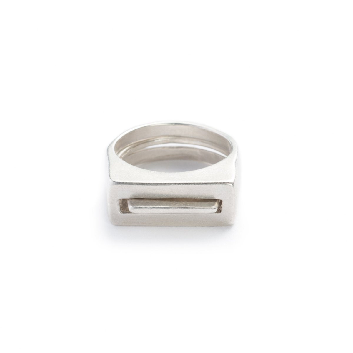 A pair of contemporary cast-silver rings, featuring one thin ring with an elongated curve (Tuyo) fitted through a chunky ring with a rectangular cutout (Mía). Hand-crafted in Portland, Oregon.