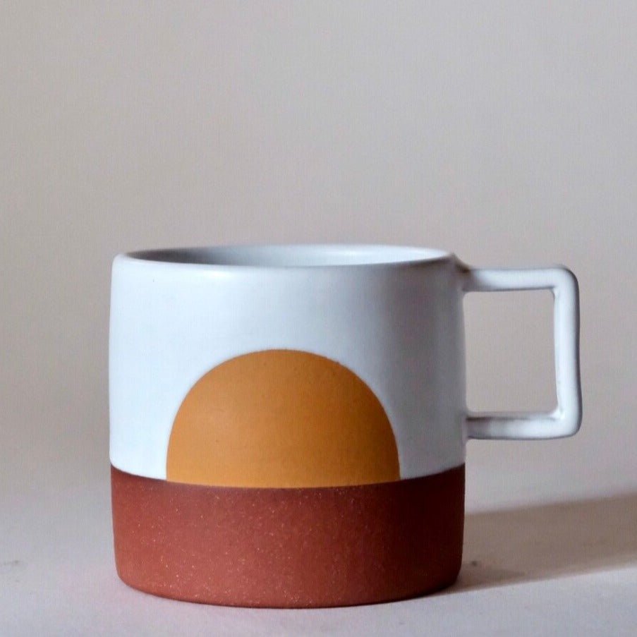 A white glazed mug with a golden yellow sun rising in the center. The base of the mug is not glazed; a matte burnt red stoneware. Made in Portland, Oregon by Sarah Wolf of Wolf Ceramics.