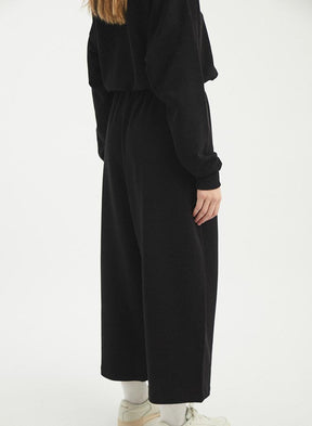 A model shows the back side of a wide leg loose fitting pant that features and elastic tie waistband. The Wanda Pants in Black are are designed by Rita Row and made in Girona, Spain.