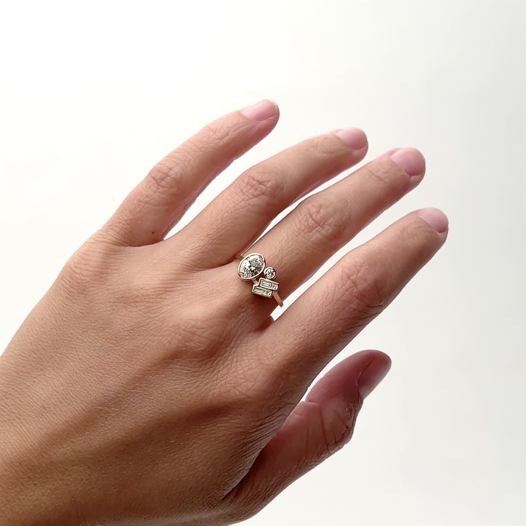 A 14k narrow band gold ring with one large oval lab grown white diamond, two baguette diamonds and one small round diamond all in a bezel setting. The Laetus ring is designed and handcrafted in Portland, Oregon.
