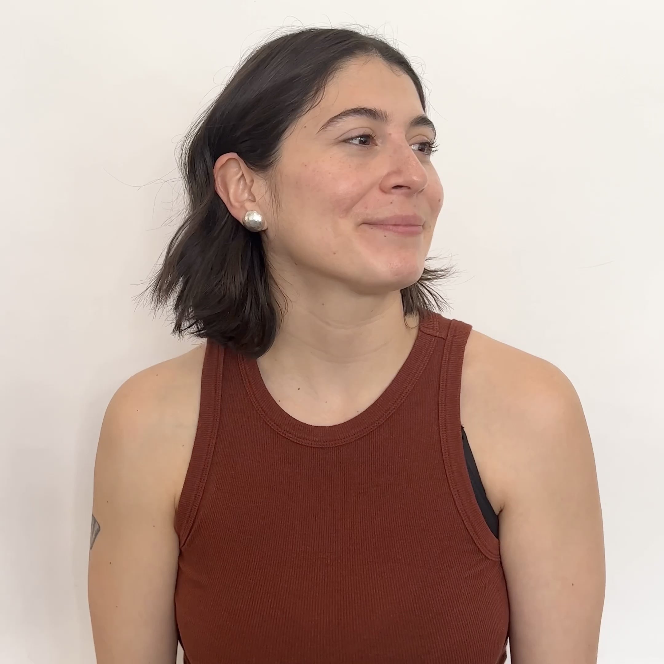 A model wears a circular and rounded hand hammered sterling silver stud earring. They turn their head from left to right. The Sentia Earrings are designed and handcrafted in Portland, Oregon.