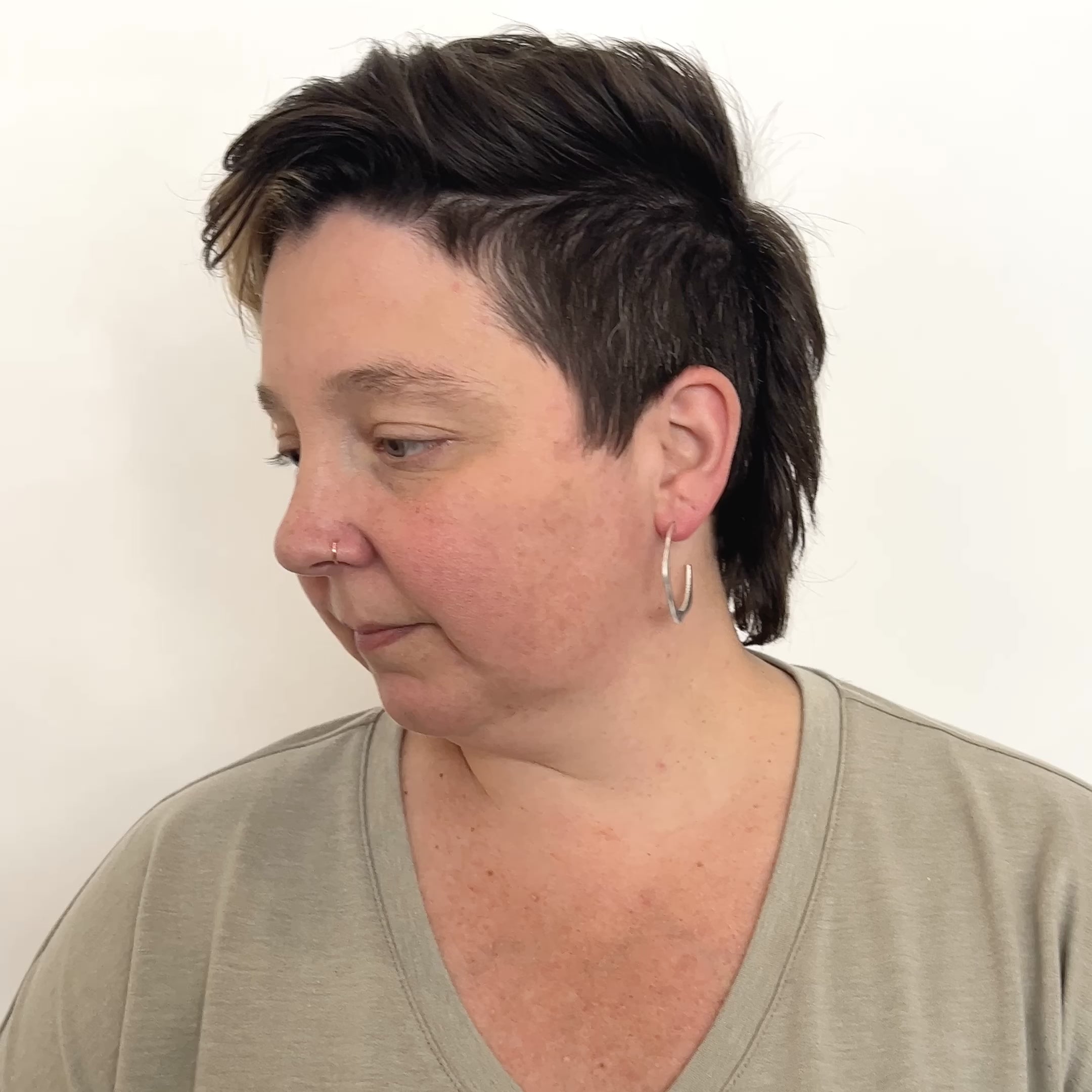 A model wears a small brass hoop earring in a wave design with a hand hammered texture and sterling silver earring posts. They shake their head from side to side to show the movement of the hoop. The small Doble Hoop Earrings are designed and handcrafted in Portland, Oregon.