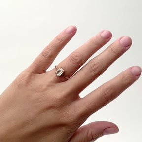 A model wears an 1.1ct. emerald cut white diamond bezel set 14k yellow gold ring. There are cut outs on the north and south of the setting. Designed and handcrafted in Portland, Oregon.